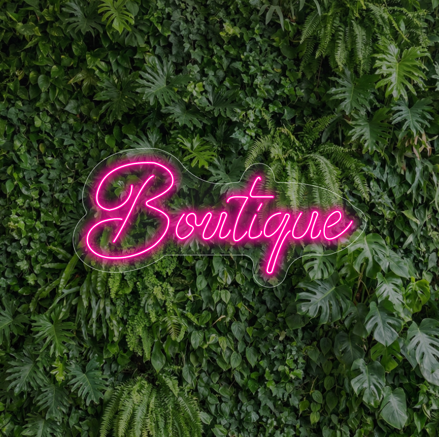 Neon z napisem "Boutique" na tle ścianki z liści
