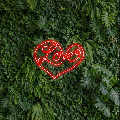 Neon w kształcie serca z napisem "love" na tle ścianki z liści